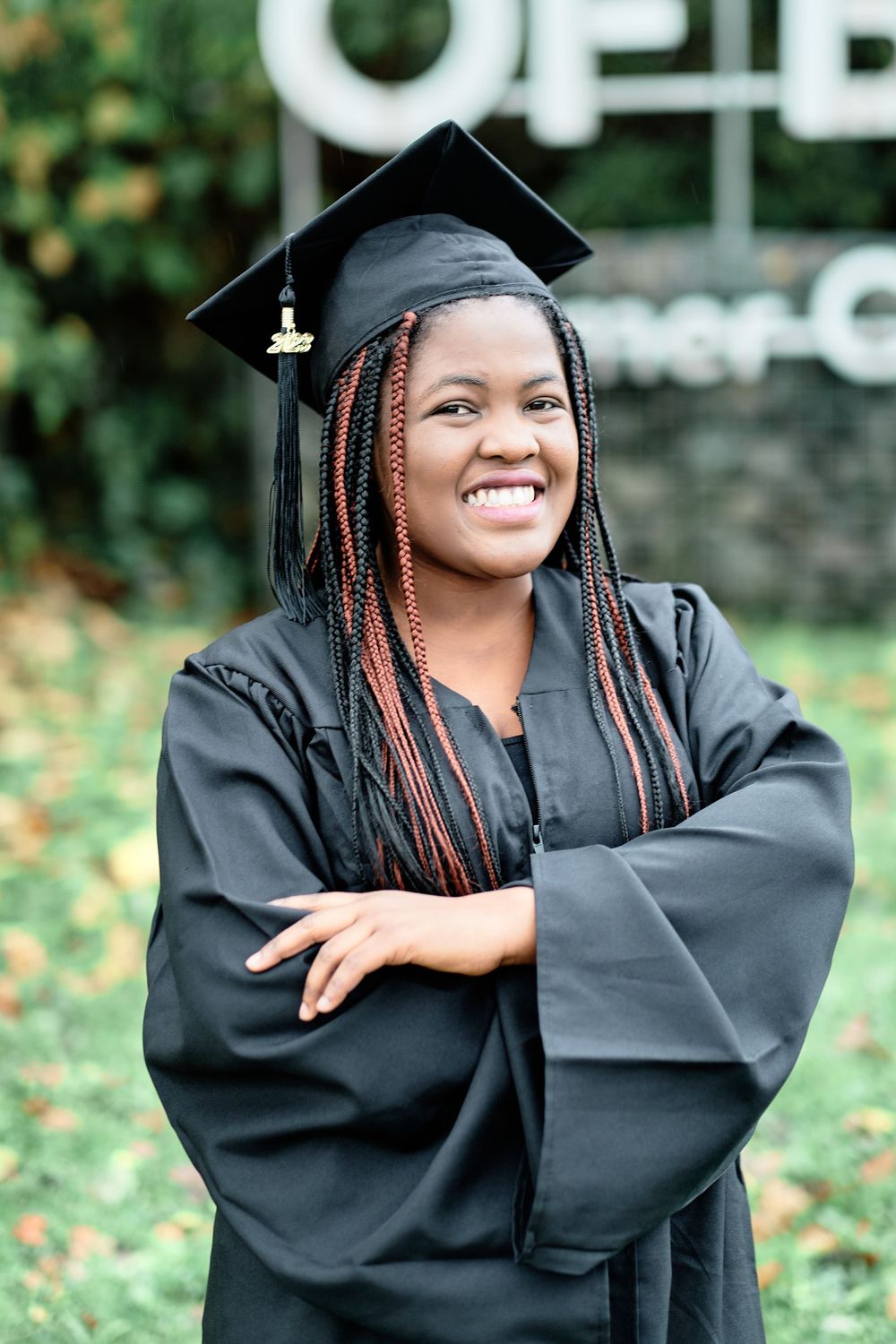 Graduate wearing black academic dress and mortarboard poses with bright smile outdoors.