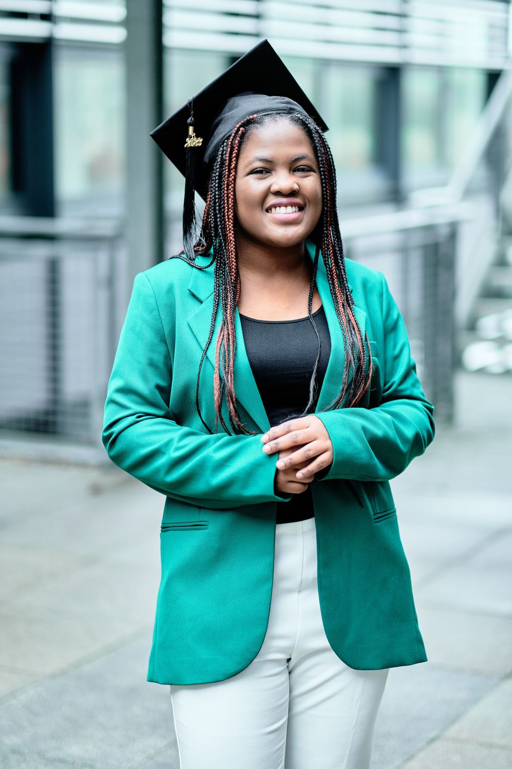 Graduate in bright green blazer and graduation cap smiles brightly during outdoor photoshoot.