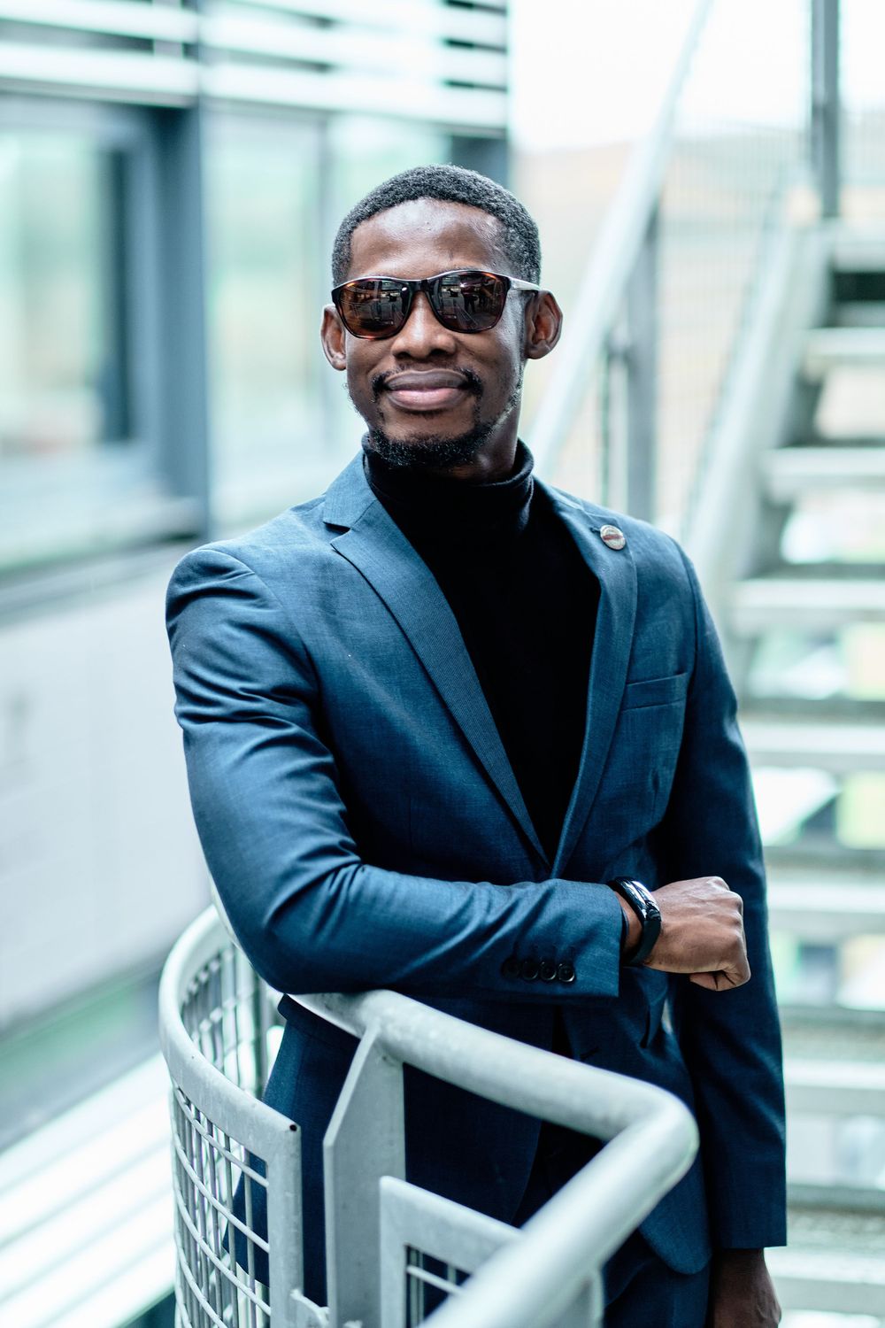 Professional wearing navy blazer and sunglasses poses confidently against modern architecture.
