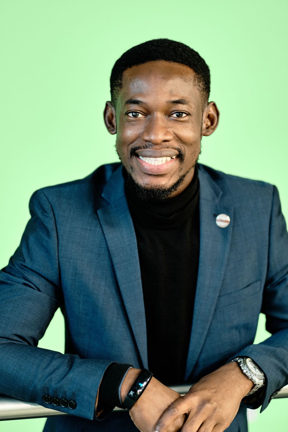 Professional in navy blazer and black turtleneck smiles against green background.
