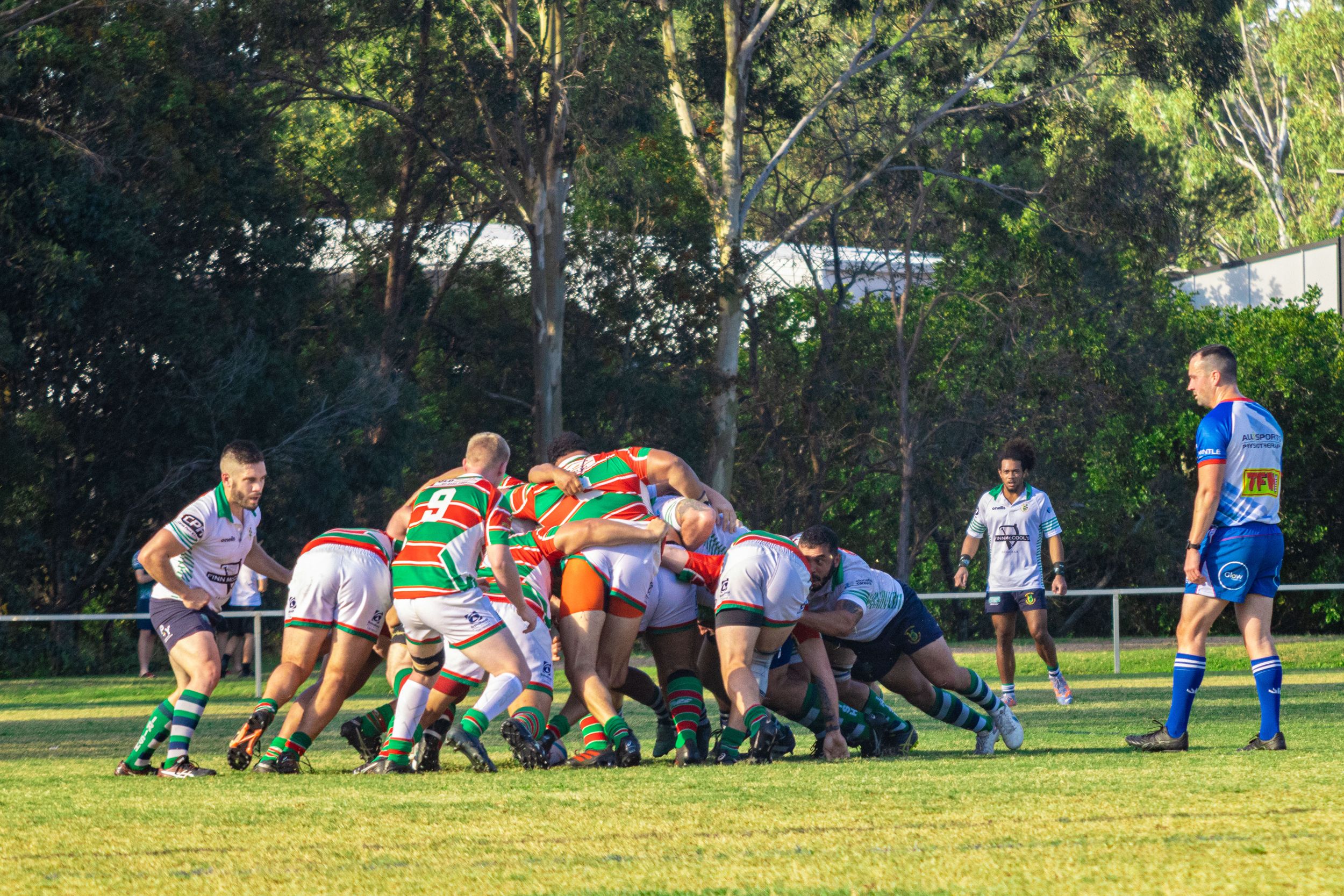 Rugby scrum formation during daytime match with players pushing against each other.