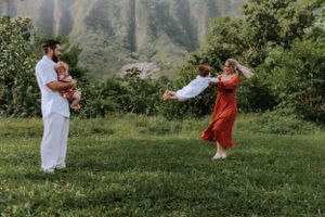 Family playing and running together on green grass with mountains in the background.