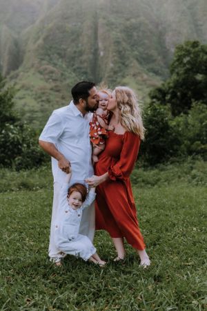 Candid family moment captured in a grassy field with dramatic mountain backdrop.