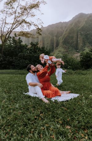 Family playing and lifting children in the air with mountain scenery behind them.