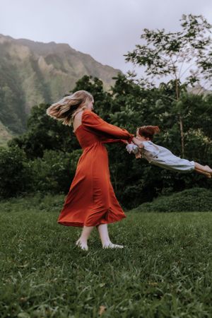 People in white and rust outfits dancing and twirling in a grassy field with mountains behind them.