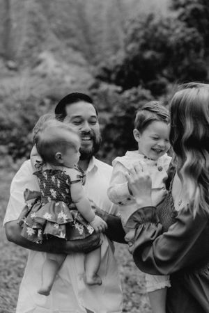 Black and white photo of a family sharing sweet moments and kisses outdoors.