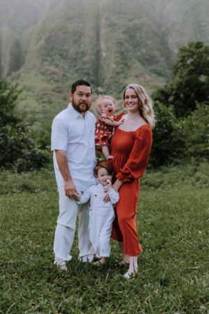 Family portrait in coordinating white and rust outfits standing together in a mountain meadow.