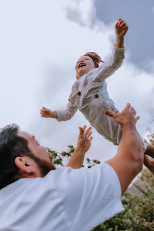 A joyful moment captured as a child is tossed playfully into the air against a blue sky background.