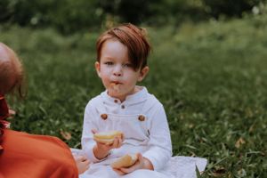 Young child in white shirt enjoying snack during outdoor family picnic.