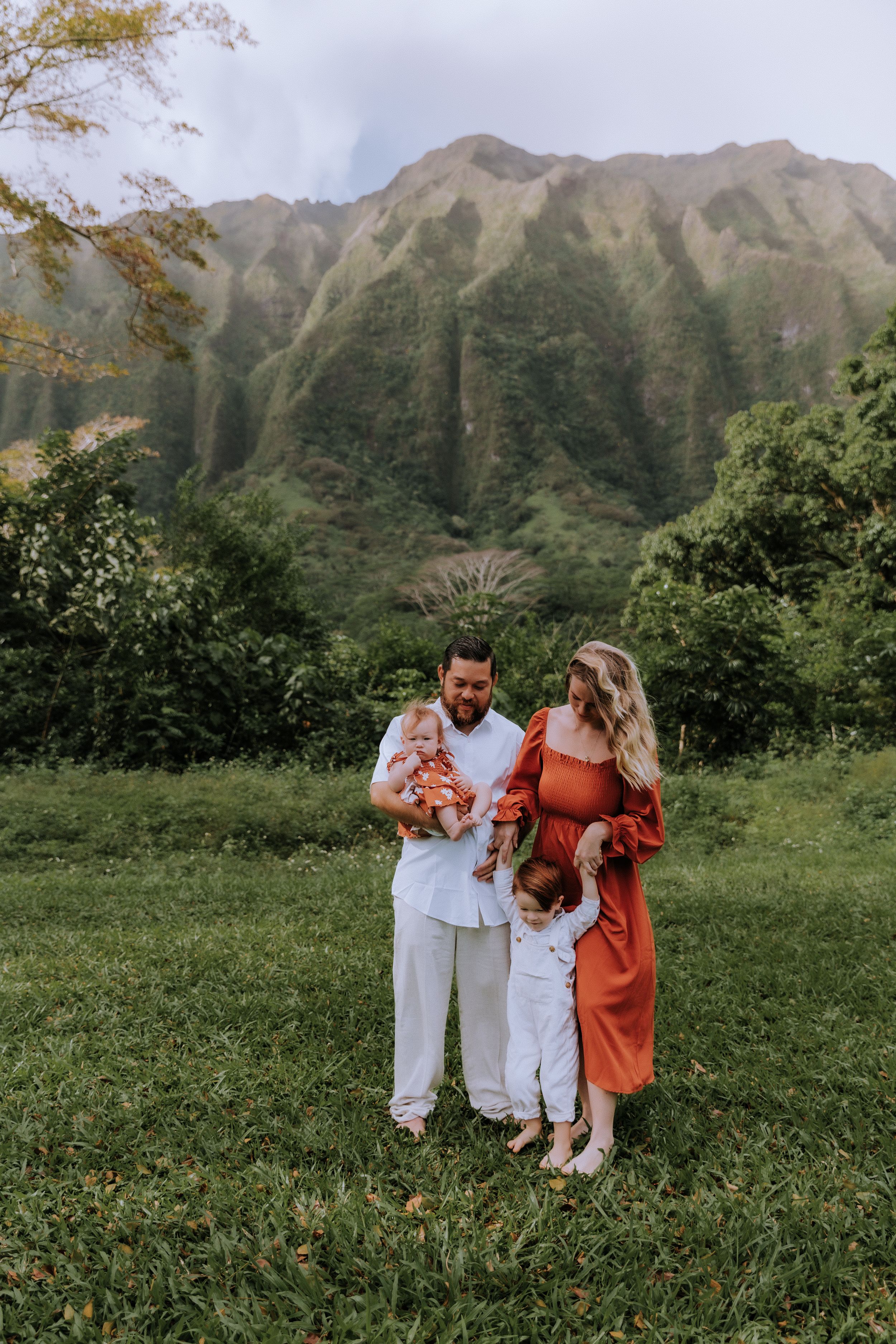 Family portrait session in front of lush Hawaiian mountains with parents and children in coordinated outfits.