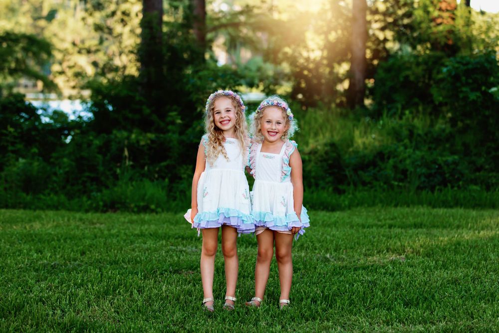 Two girls in matching light blue dresses stand together on grass during golden hour.