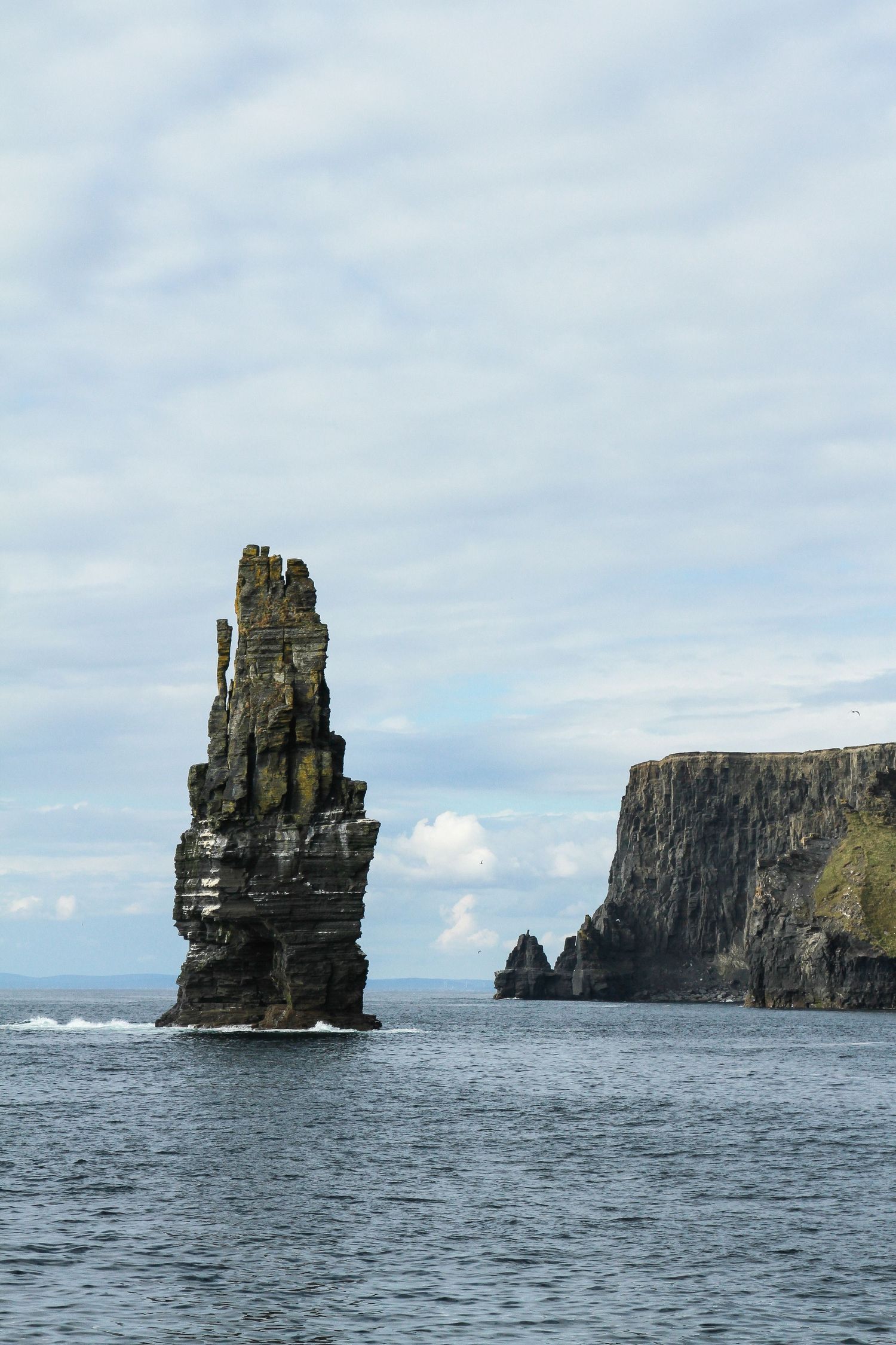 Cloudy day at the Cliffs of Moher, Ireland. The ocean crashes against towering cliffs.