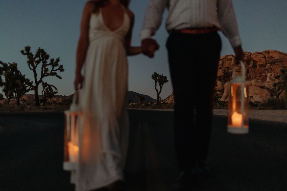 couple holding lanters for engagement joshua tree photos walk hand in hand with a white dress