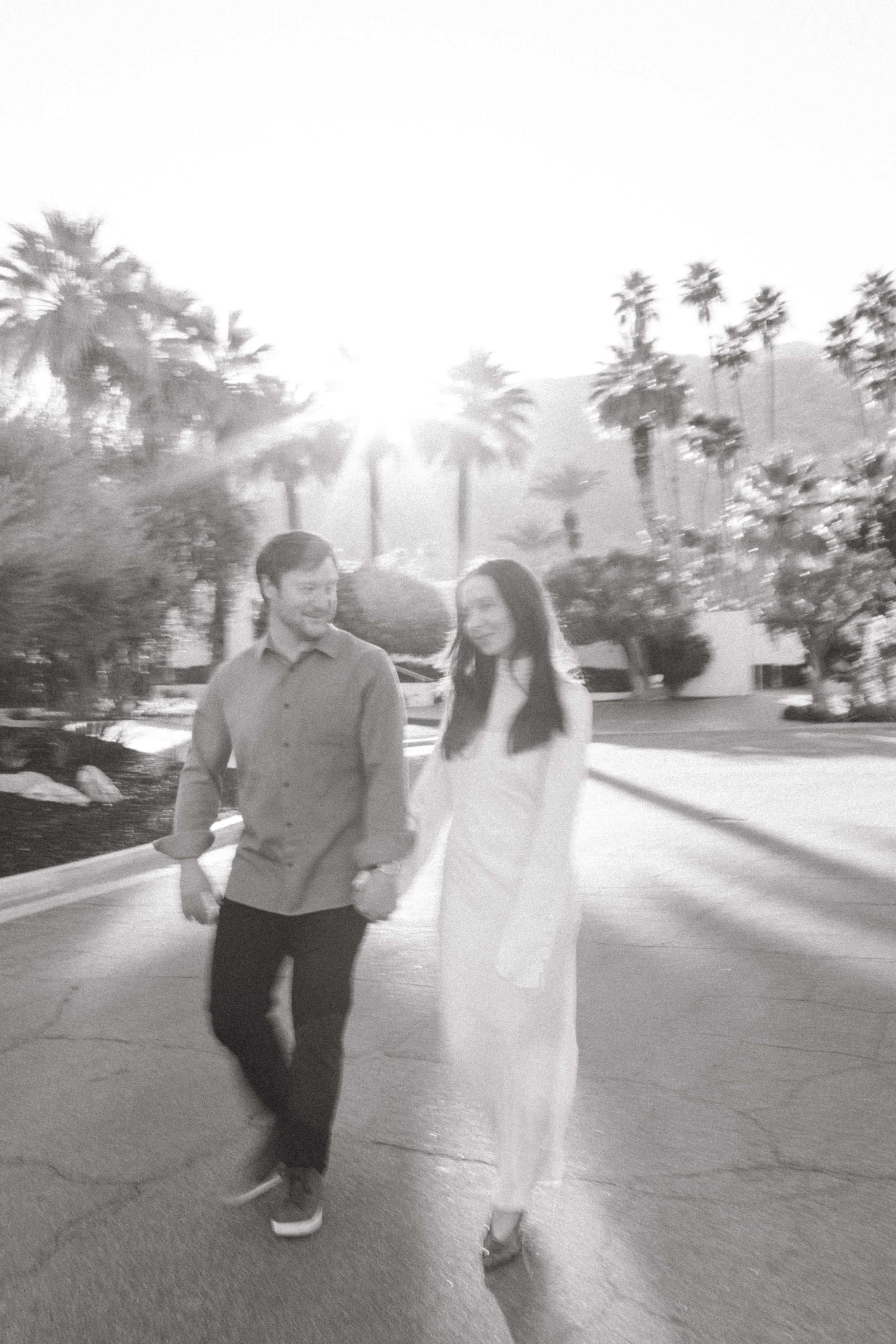 a black and white photo of a man and woman walking down the street in palm springs for an engagement photoshoot