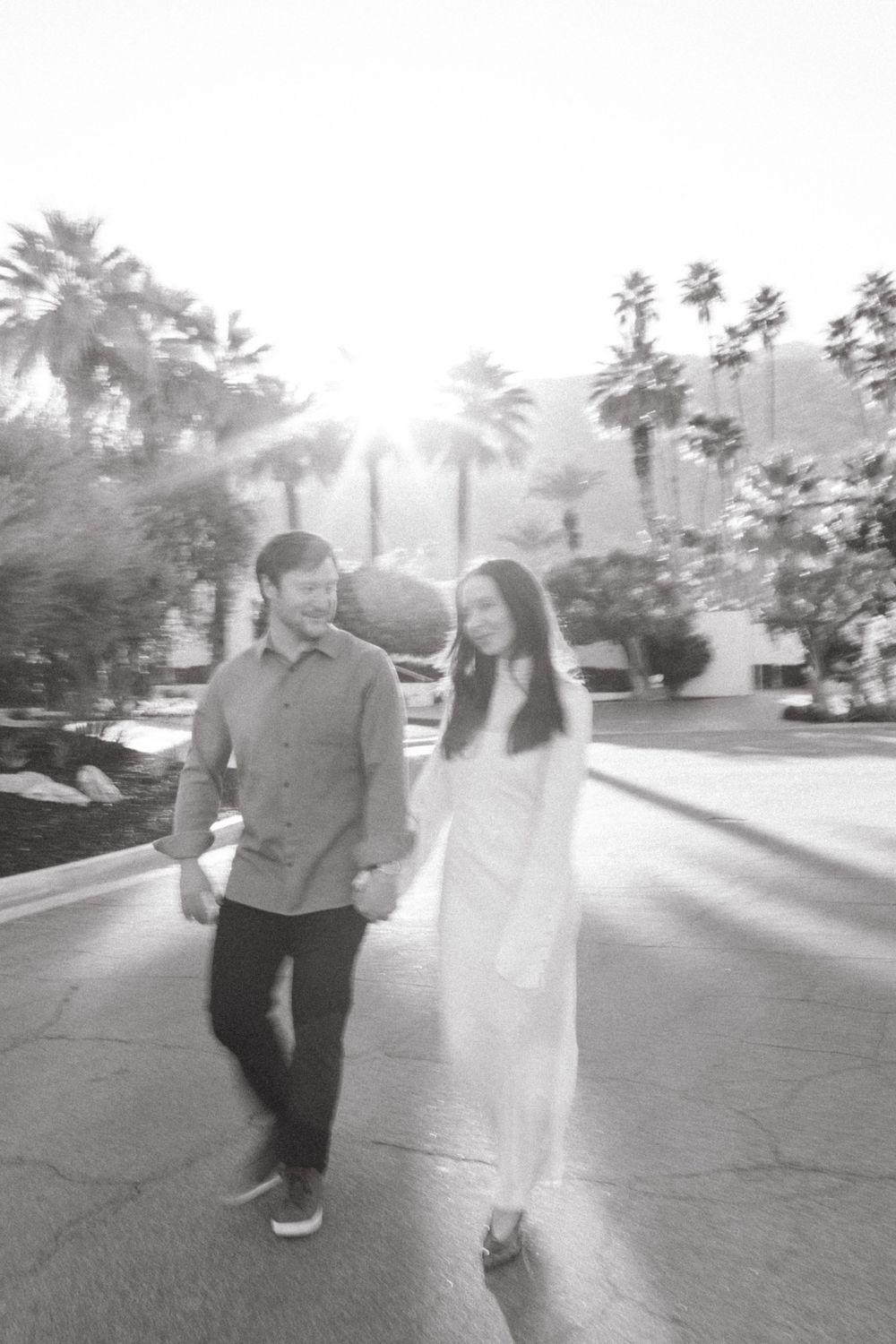 a black and white photo of a man and woman walking down the street in palm springs for an engagement photoshoot