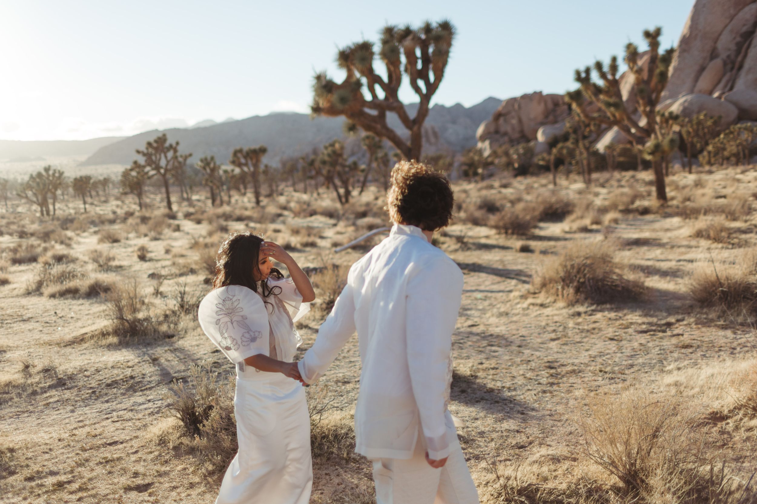 couple frolicks in white garments and across the joshua tree desert for their elopement photos