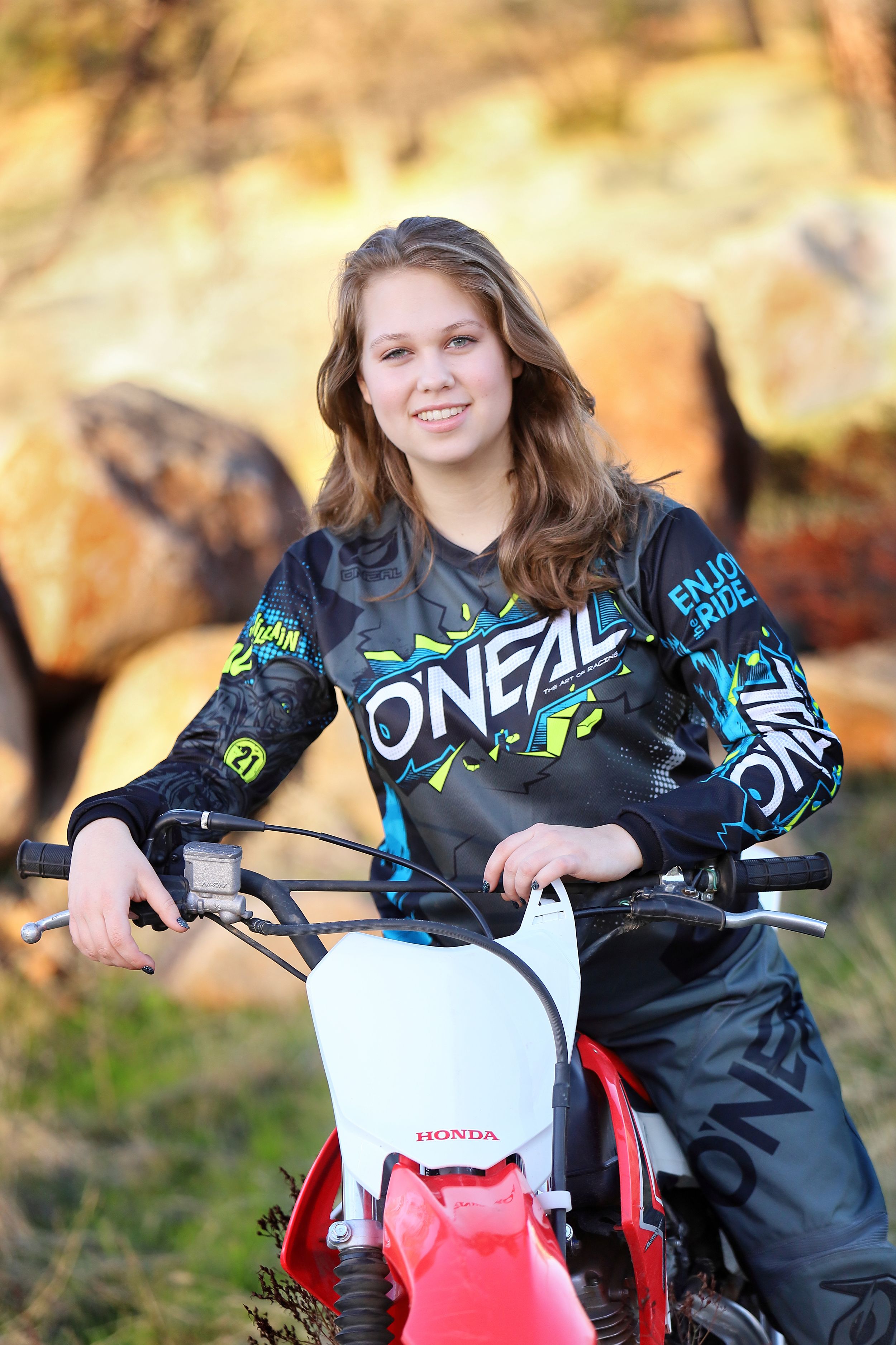 Dirt bike rider in O'Neal gear poses with Honda motorcycle in autumn setting.