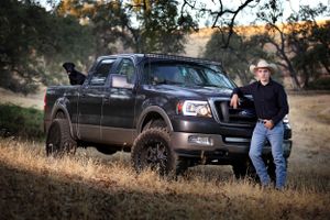 Modified black Ford F150 truck parked on a hill with rugged off-road tires and customizations.