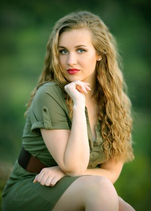 Portrait of a woman in olive green top with flowing curly hair against a blurred natural background.