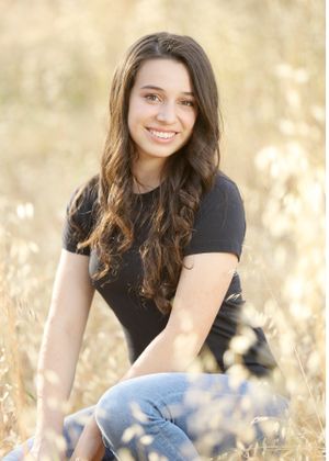 Woman in black shirt and jeans sits in golden sunlit field.