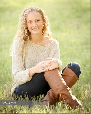 Person in cream sweater sits on grass wearing brown riding boots.