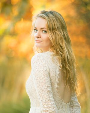 Portrait of a woman in white lace dress with golden sunlit backdrop.