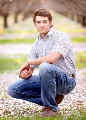 A casual outdoor portrait in a field with white flowers and trees in the background.