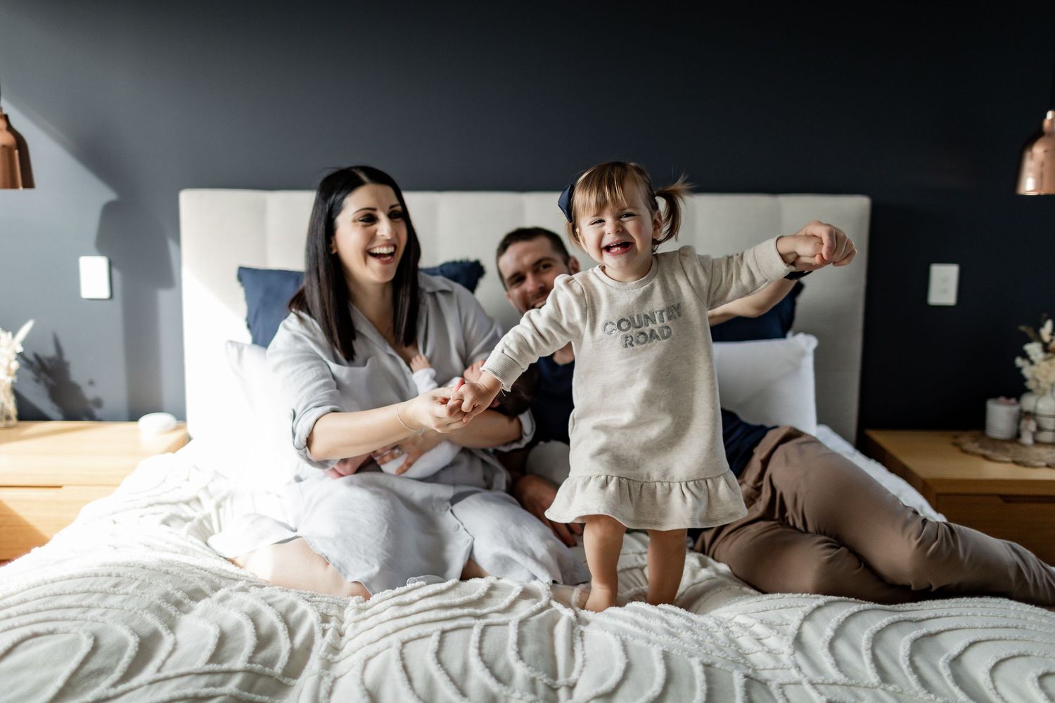 A joyful family moment captured on a bed with white textured bedding.
