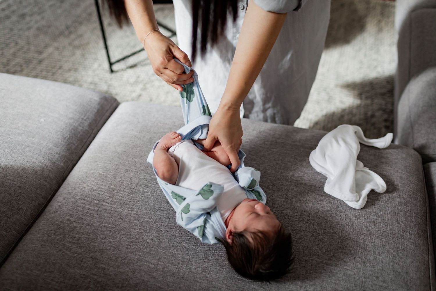 Changing a baby's diaper on a gray couch with tissues nearby.