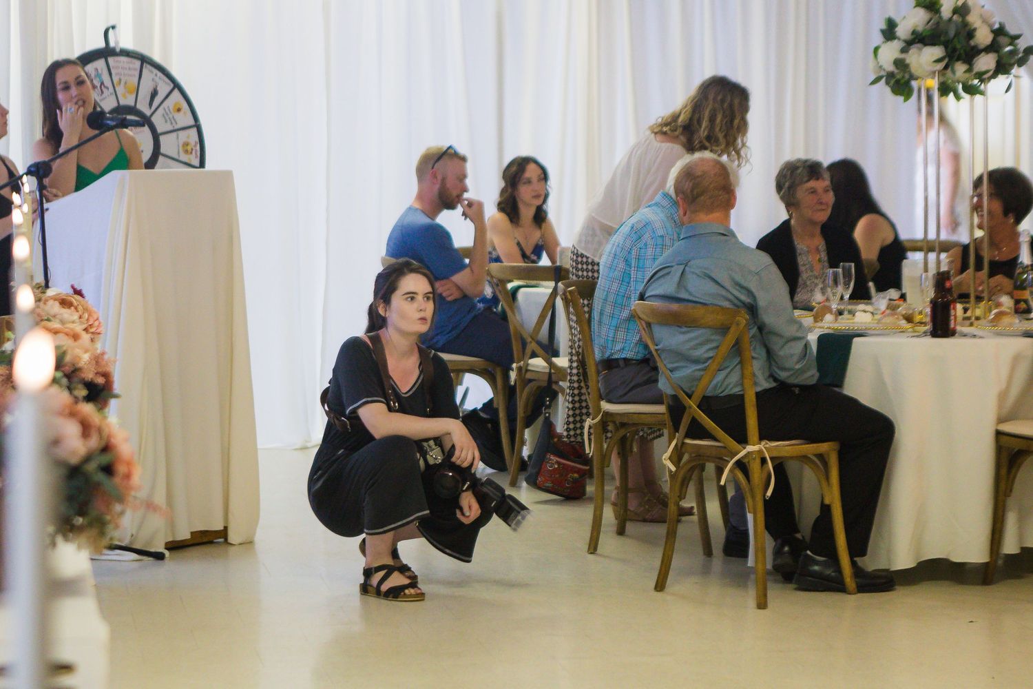 A photographer crouches to capture photos at an indoor wedding reception.