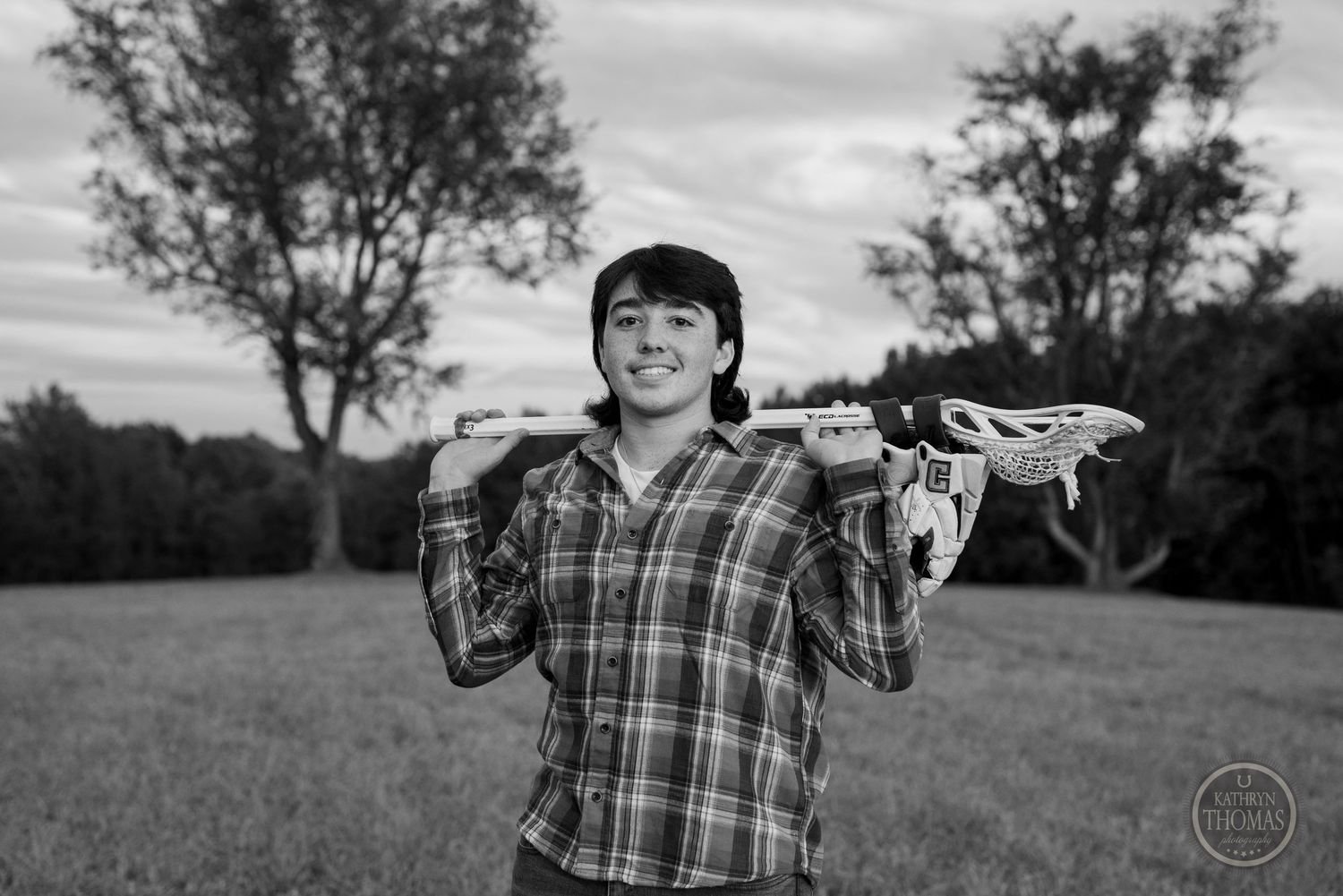 Black and white image of person holding lacrosse stick over shoulders in field.