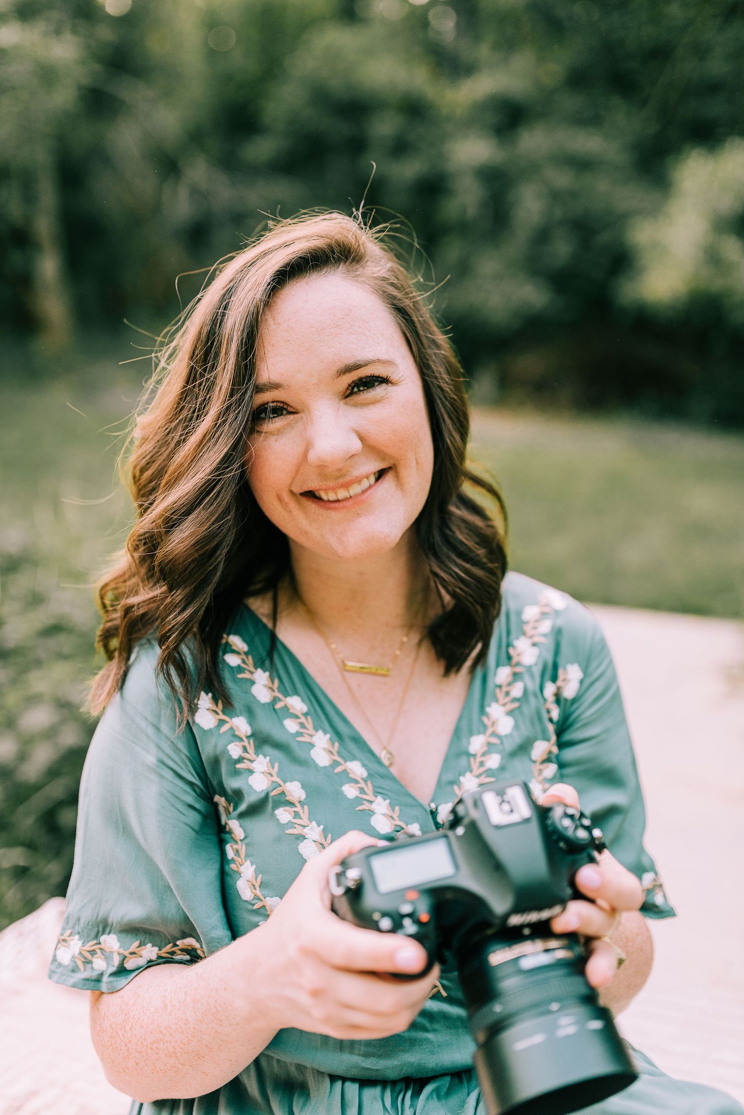 Photographer wearing a green dress, holding her camera and smiling