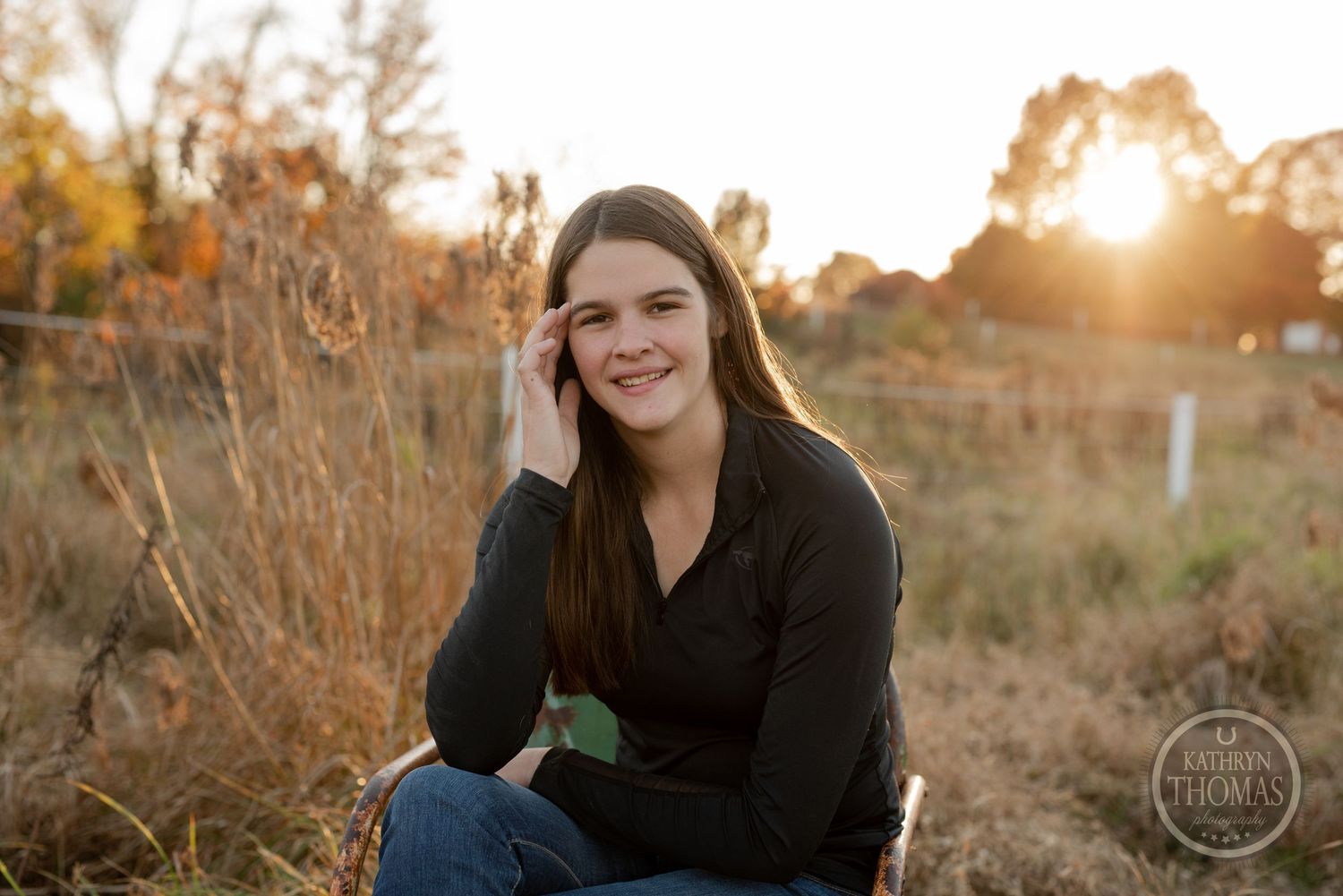 Natural light portrait at sunset with tall grass and fence.