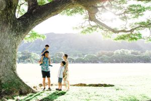 Family enjoying a peaceful moment under a large tree overlooking a lake and mountains in Hawaii.