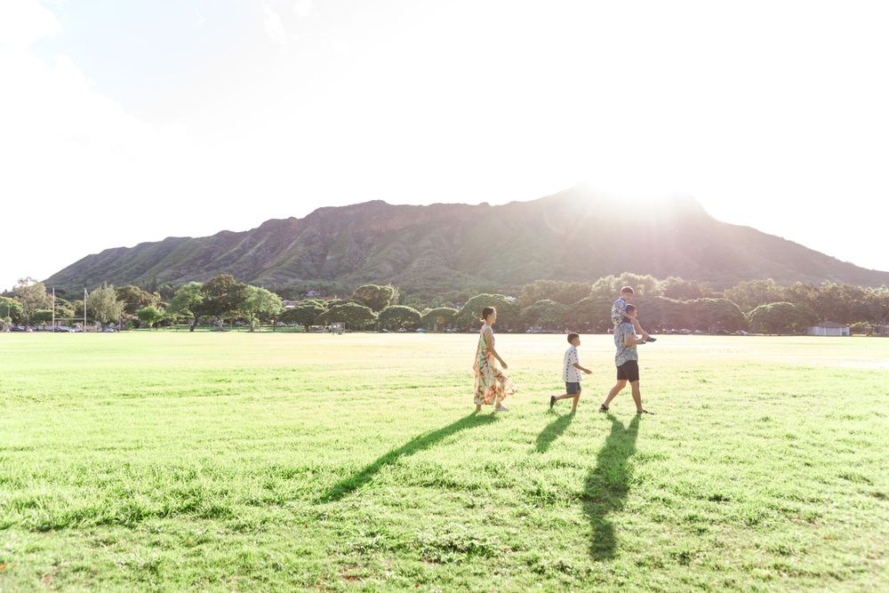 People walking together across a sunlit grassy field with mountains in the background.