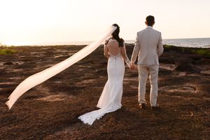 A wedding couple walks along a coastal path with a flowing veil in the breeze.
