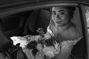 Black and white wedding portrait of bride with bouquet sitting in car.