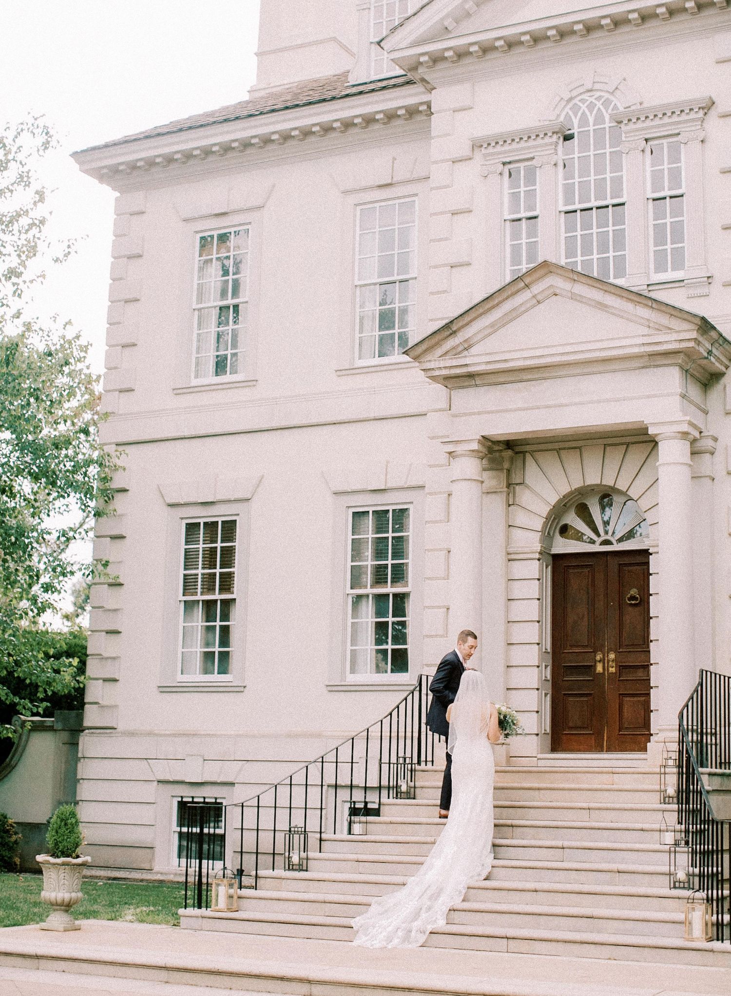 Elegant white colonial building with bride posing on front steps.