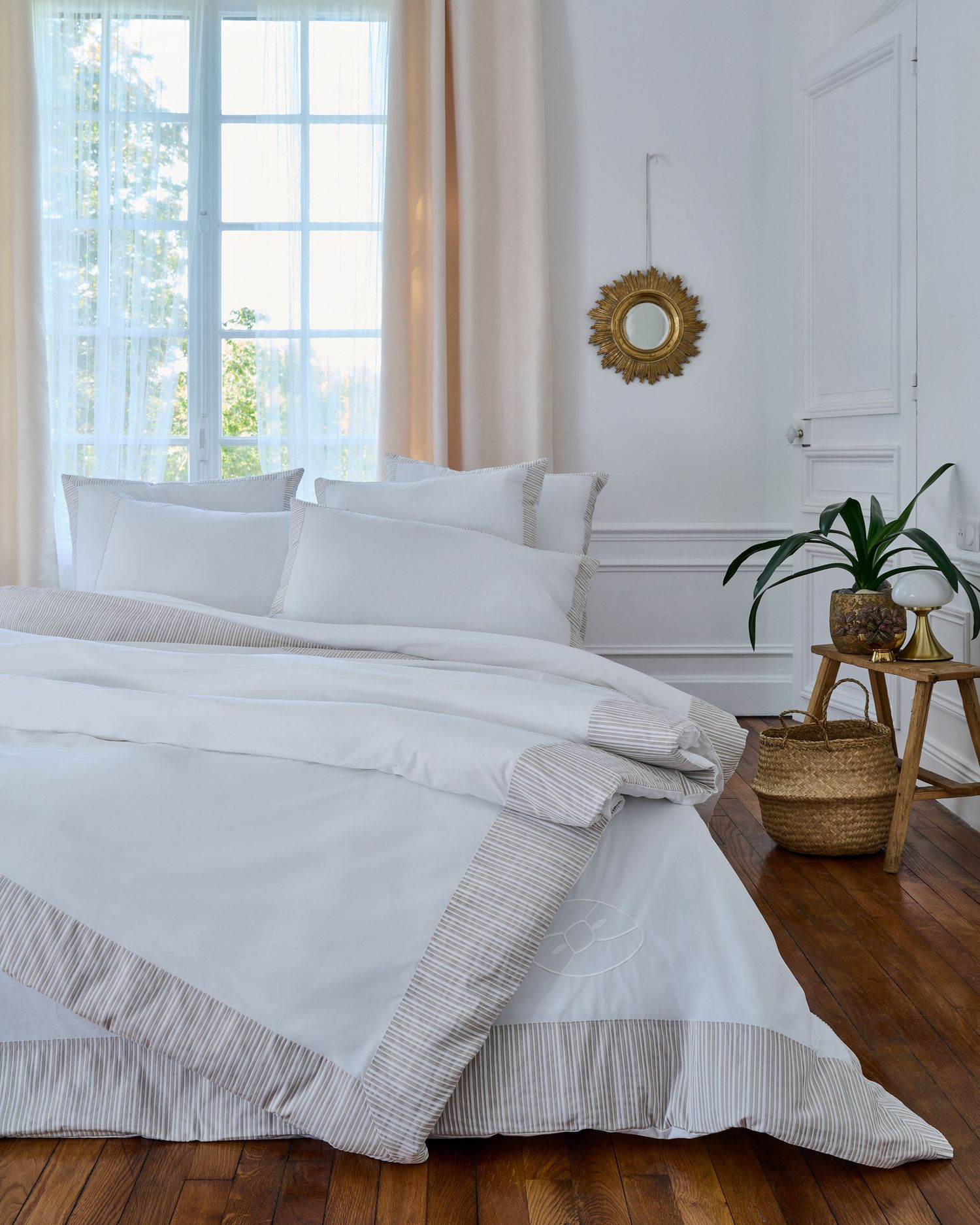 Bright white bedroom interior with sunburst mirror and woven basket decor.