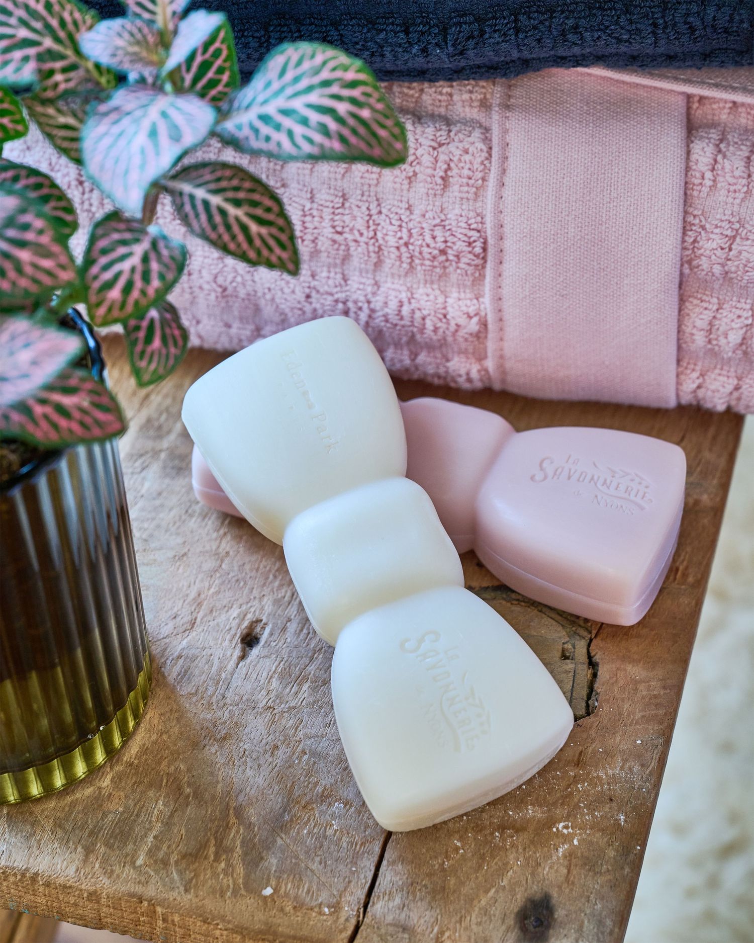 Pink and white soap bars with plant decor against pink towel background.