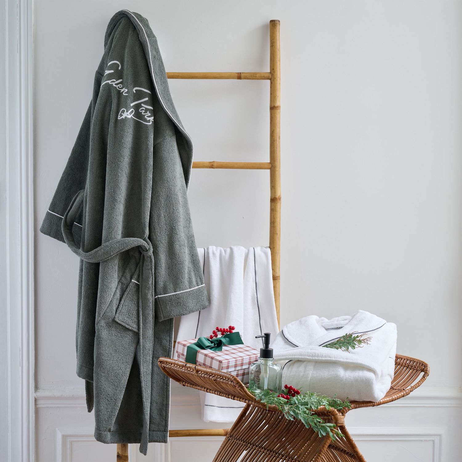 Gray bathrobe and white towels arranged on wooden ladder with holiday greenery.