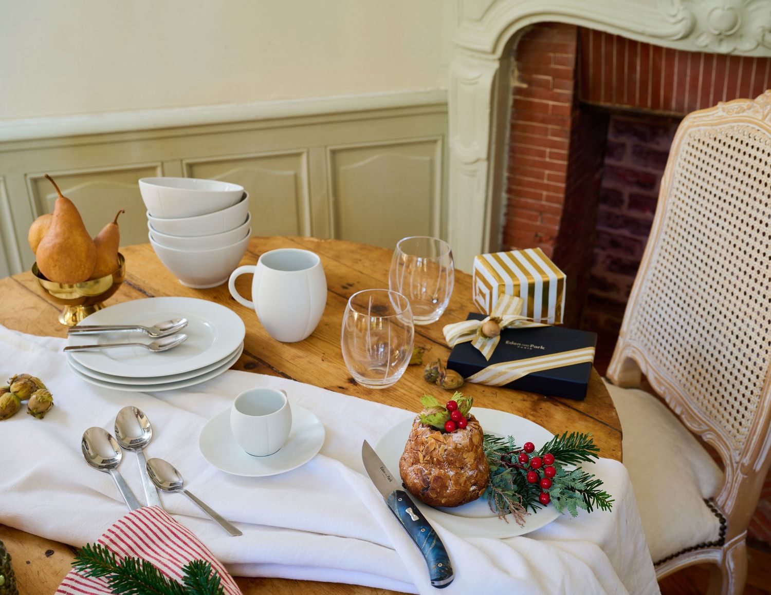 A cozy holiday table setting with white dishes, wine glasses, and festive greenery decorations.