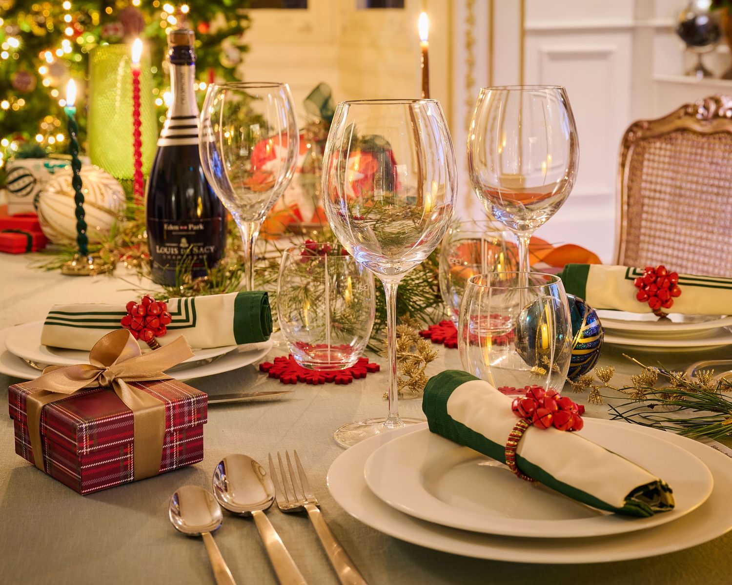 Elegant Christmas table setting with wine glasses, wrapped gifts, and red decorations.