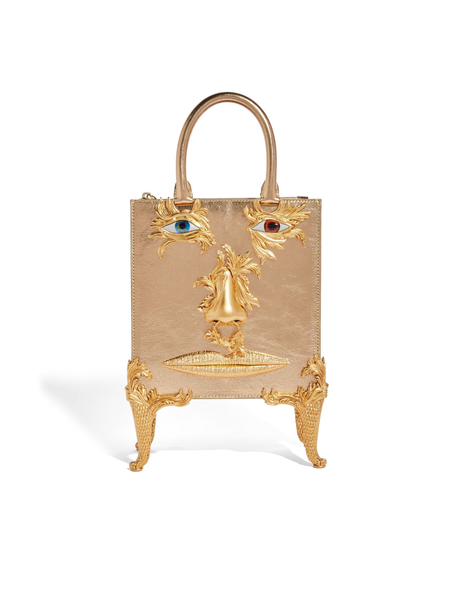 Gold metallic handbag with decorative face design featuring jeweled eyes and ornate feet.
