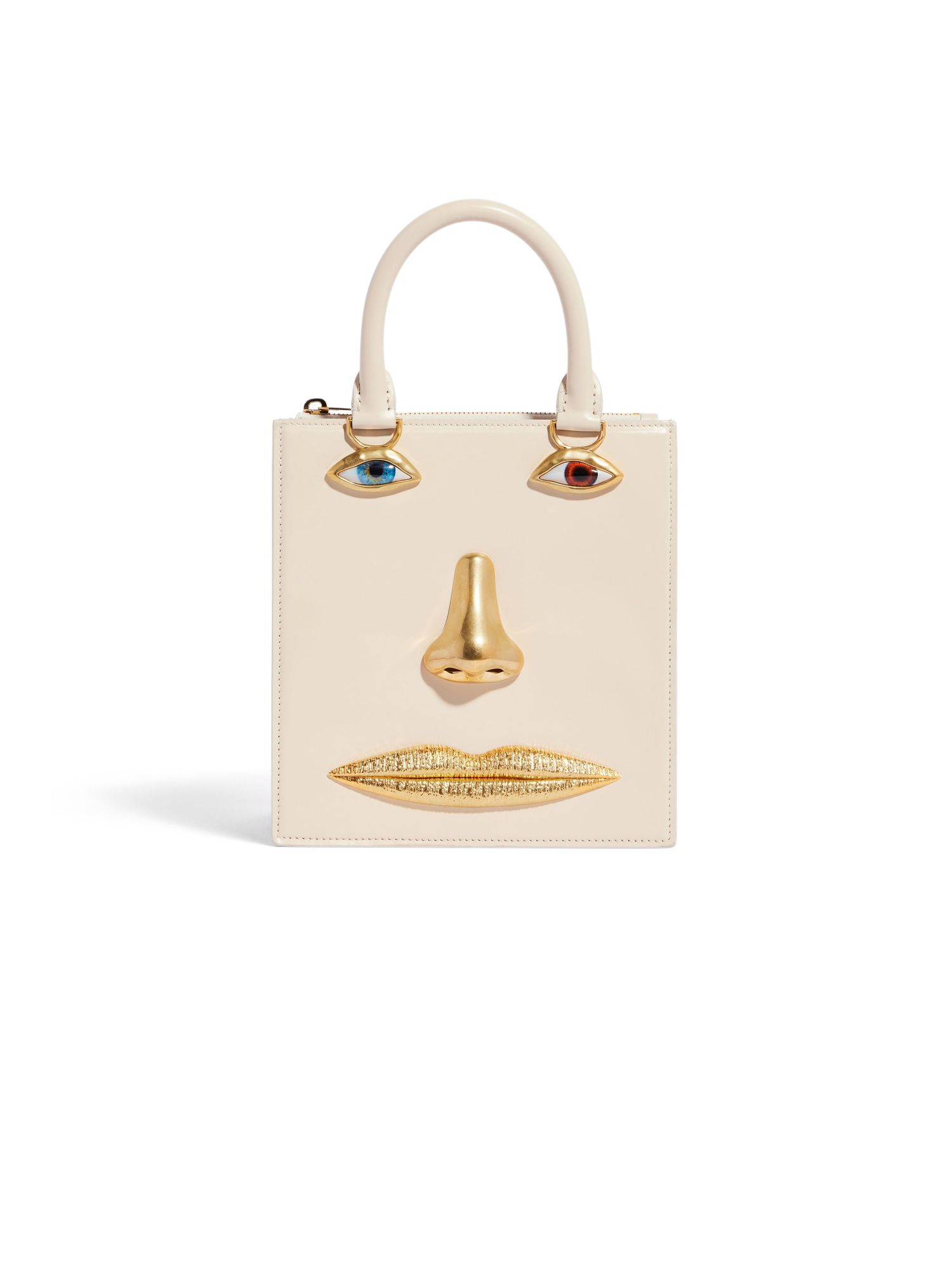 Cream leather handbag with gold facial features including eyes, nose and lips.