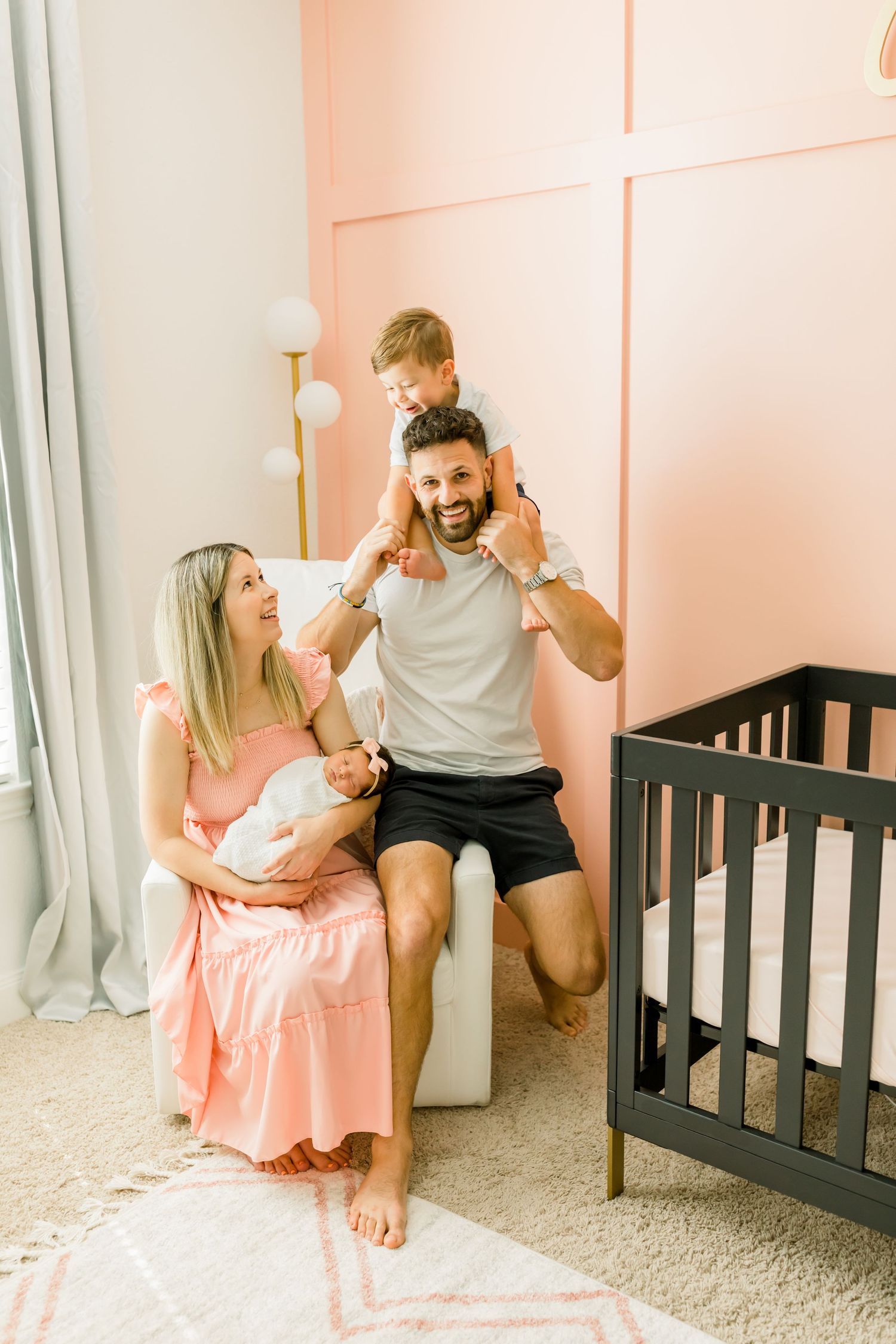 A joyful family moment in a pink nursery with father carrying child on shoulders.