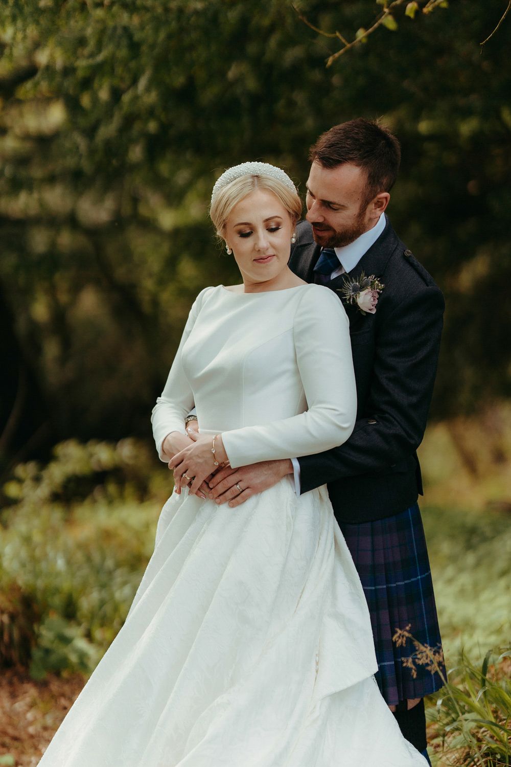 A romantic wedding moment between a couple in traditional Scottish attire with the bride in white and groom in kilt.