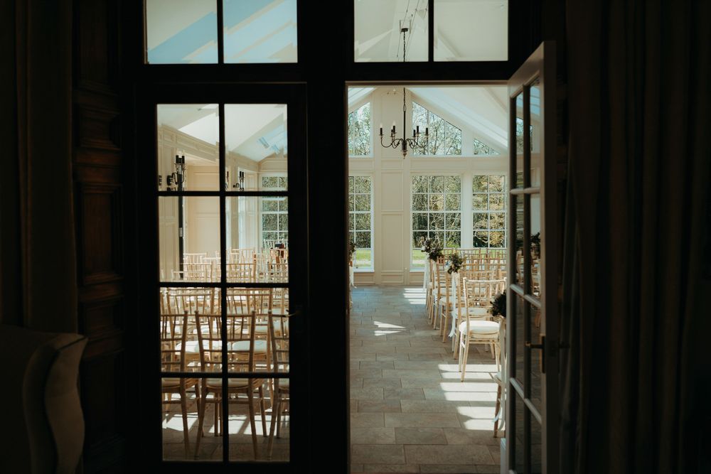 Empty chairs set up for a wedding ceremony viewed through large glass doors.