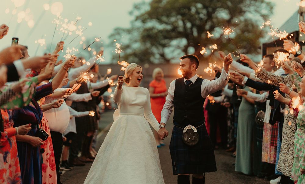 Wedding guests create sparkler tunnel for newlyweds during evening celebration.