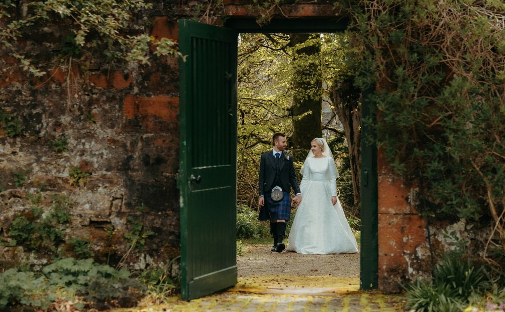 Couple walks through green garden doorway during Scottish wedding ceremony.